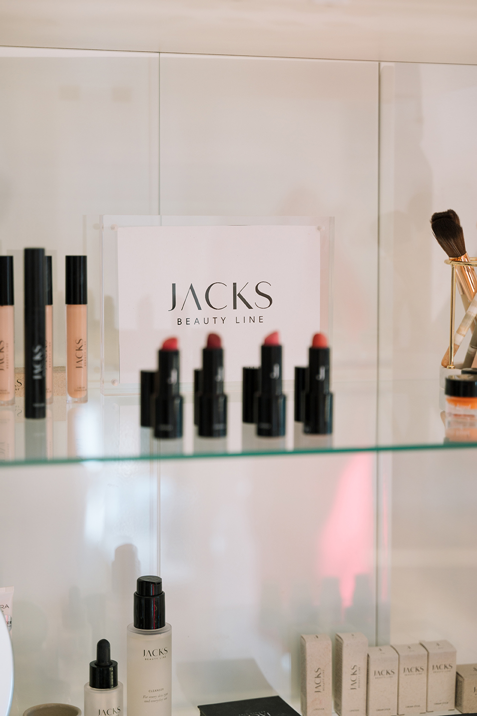 Regal: Lippenstift und Kosmetikprodukte von Jacks Beauty Line auf einem Glasregal ausgestellt.