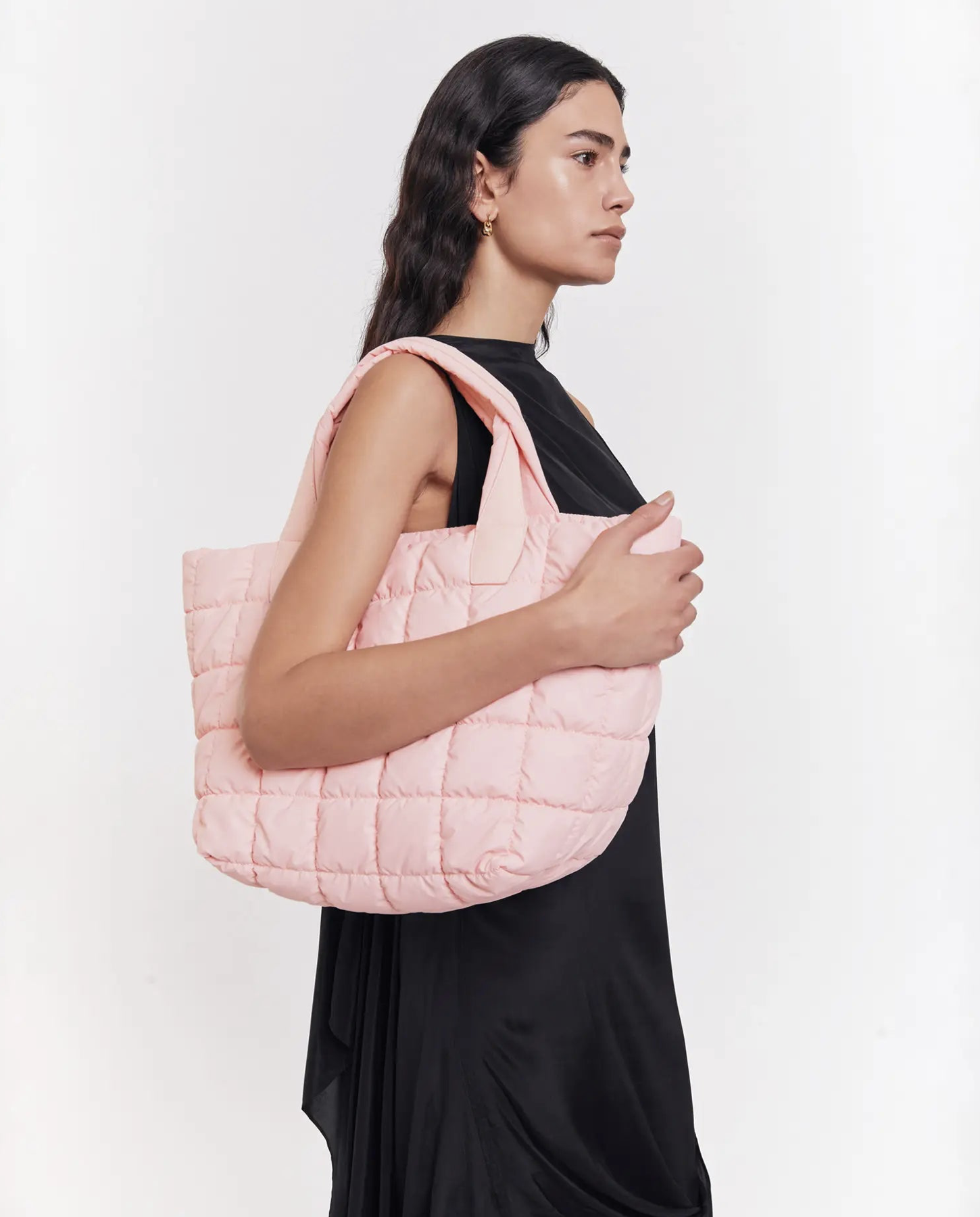 Eine Frau im Profil, neutrale Miene, schwarze Kleidung, rosa gesteppte Tasche über der Schulter.