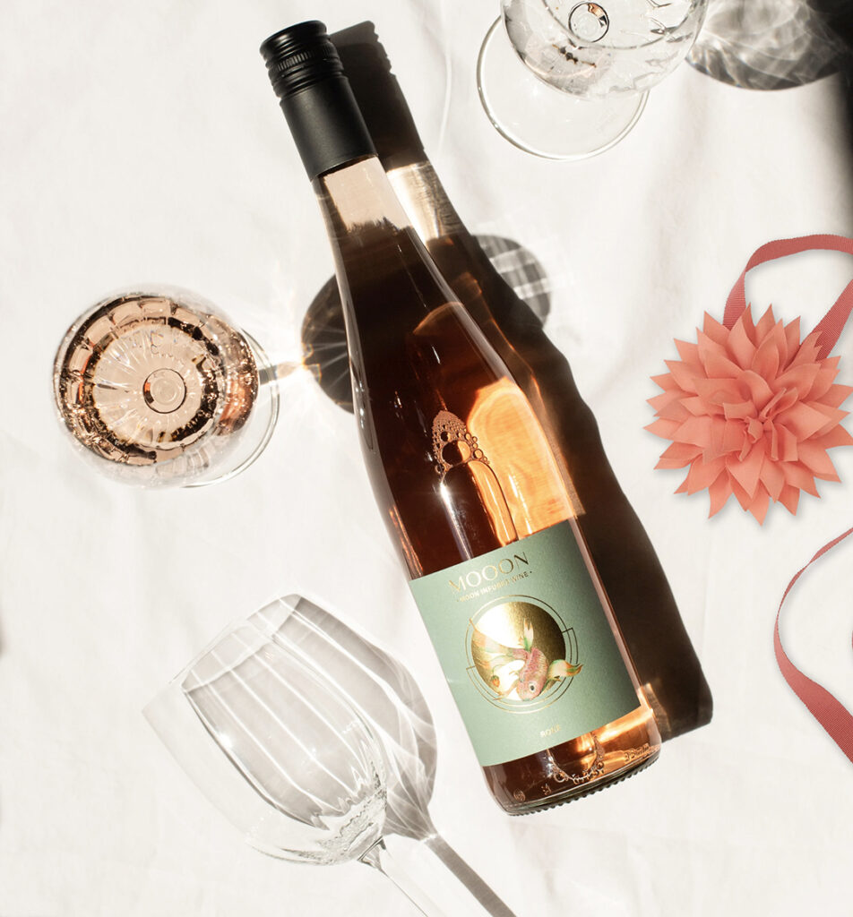 Weinflasche auf weißem Tuch mit Gläsern und rosa Geschenkband.