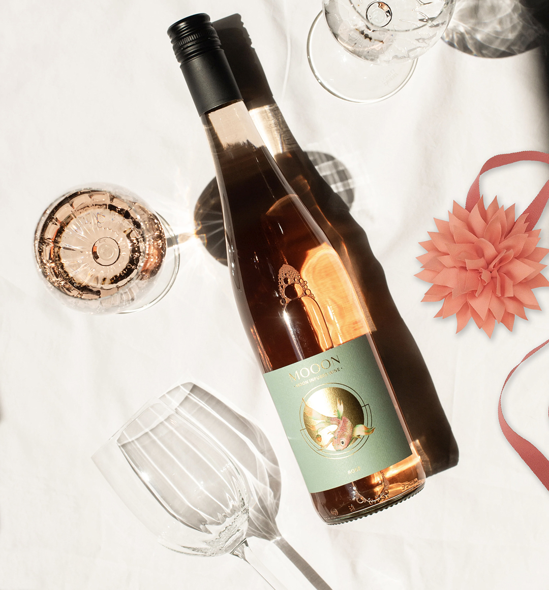Weinflasche auf weißem Tuch mit Gläsern und rosa Geschenkband.